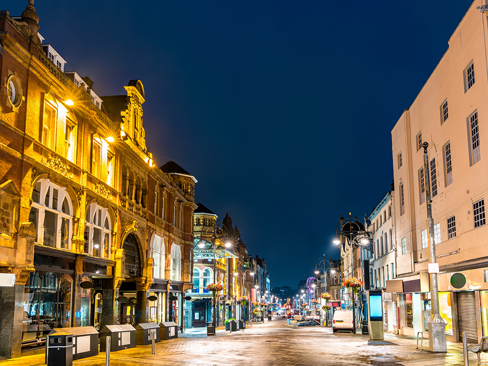 Evening shot of a lit up pedestrianised high street full of commercial properties..