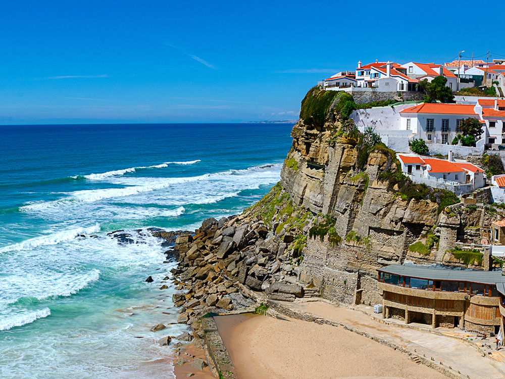 Panoramic view of Beautiful coastal view of Praia Azenhas do Mar near Sintra, Lisbon, Portugal. Rows of white houses with orange roofs line the cliffside.
