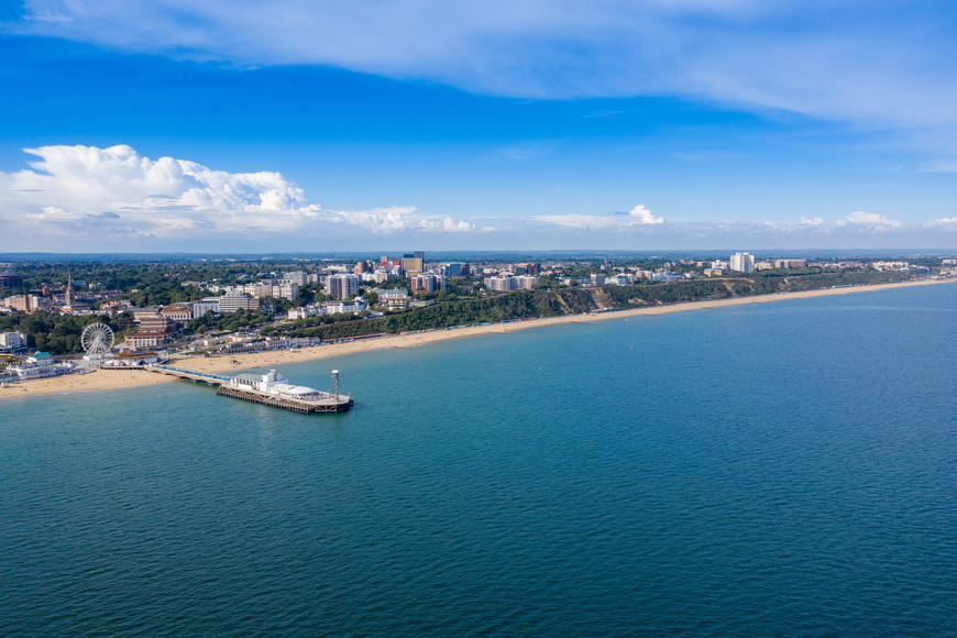Aerial view of miles of Bournemouth beach, the Observation Wheel and Pier on a beautiful sunny summers day with lots of people relaxing and sunbathing on the British Dorset sandy beach and blue sea