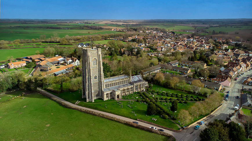 View of St Peter and St Pauls Church in Lavenham, and the surrounding properties and green countryside fields of Suffolk.