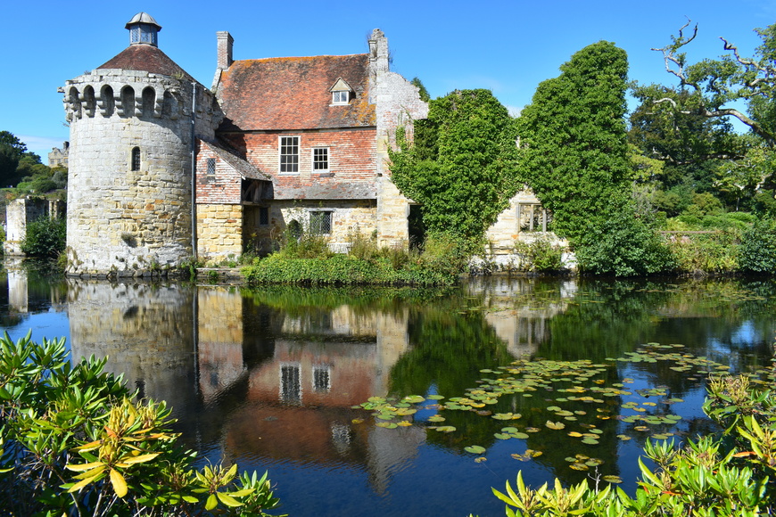 Clear sky and sunny view of Scotney Castle near Tunbridge Wells, Kent with a reflection of the castle and trees in the River Bewl