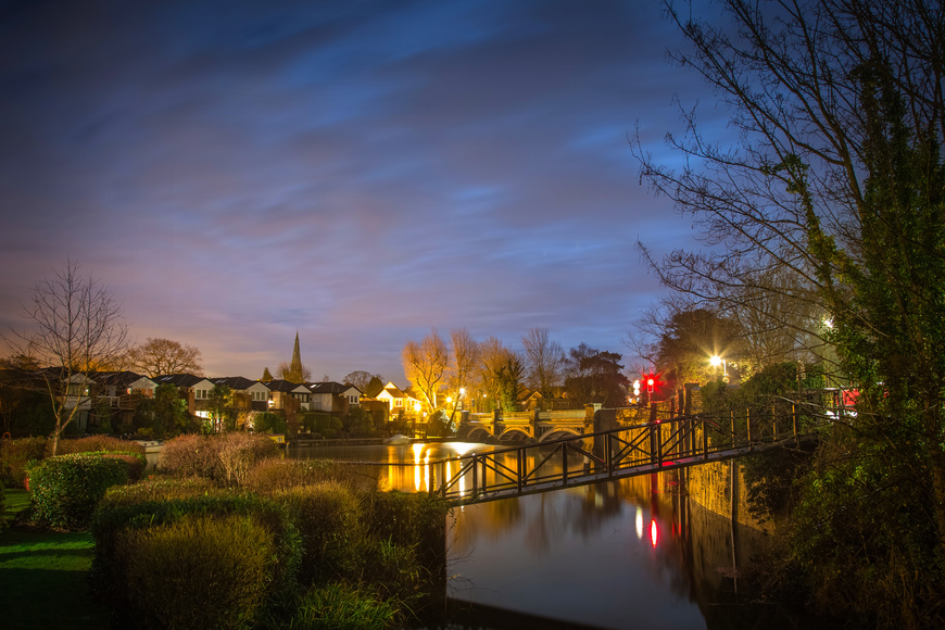 Lit up night view of Weybridge showing the properties and trees by the river