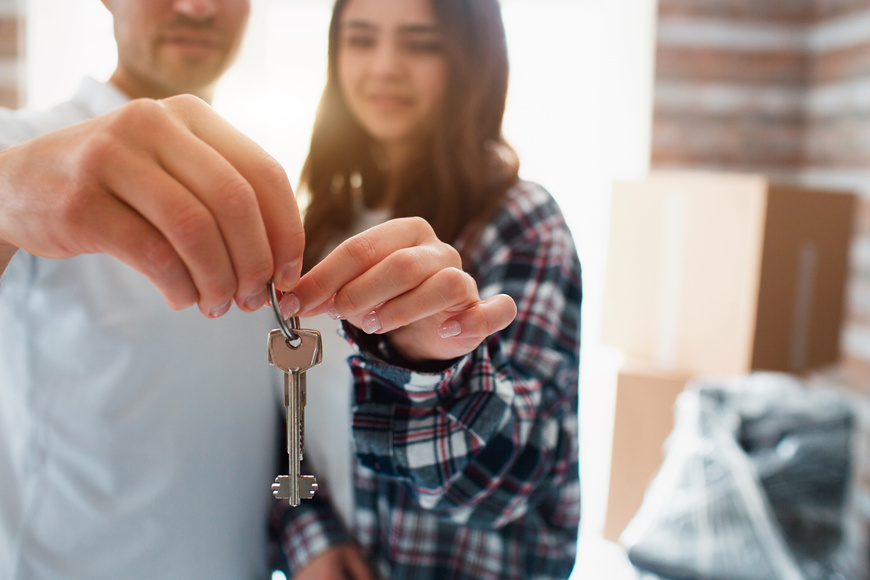 Close-up of keys in hands. Young couple first-time home owners celebrate moving day standing near boxes in new own house.