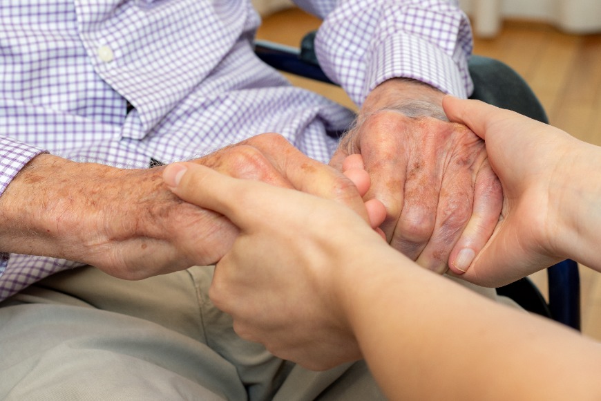 Elderly person and younger carer holding hands in a care home.