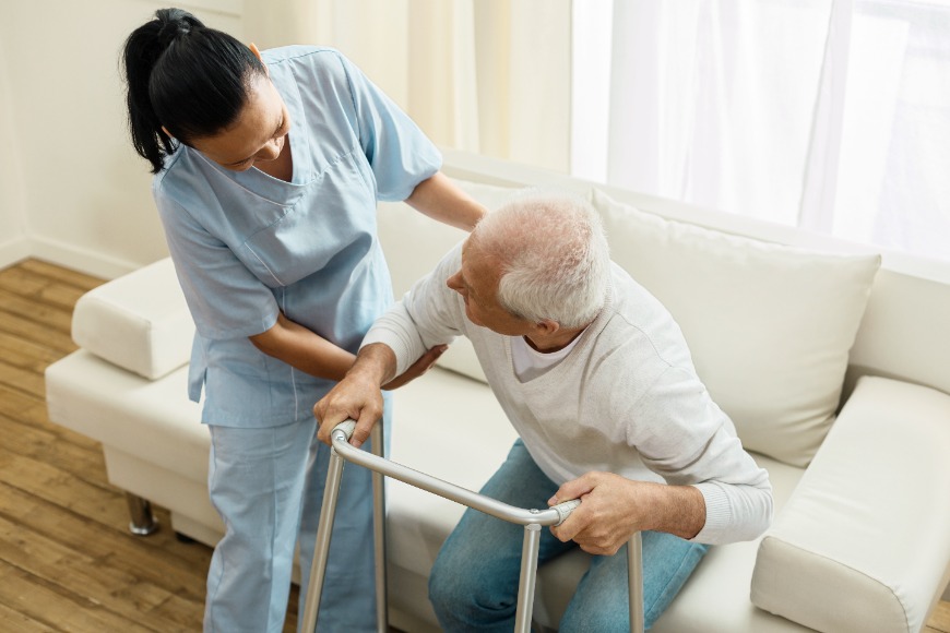 Pleasant & friendly caregiver helping an elderly gentleman to stand in a care home.