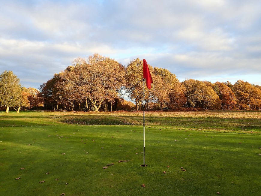 Flag in hole on green at golf course in autumn sun, Chorleywood, Hertfordshire