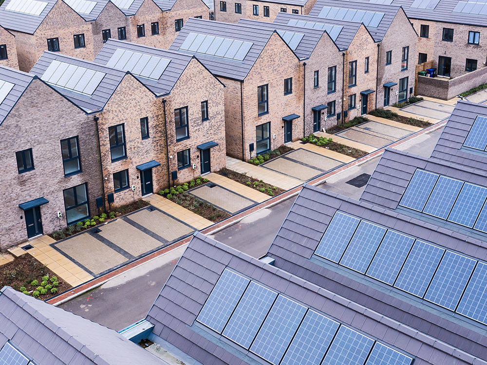Colour photo displaying street with new build housing development. Three rows of very similar new houses with solar panels.
