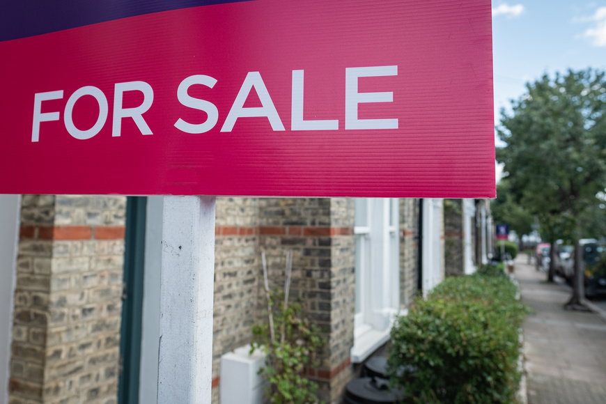 Estate agent's For Sale sign outside a residential property on a street
